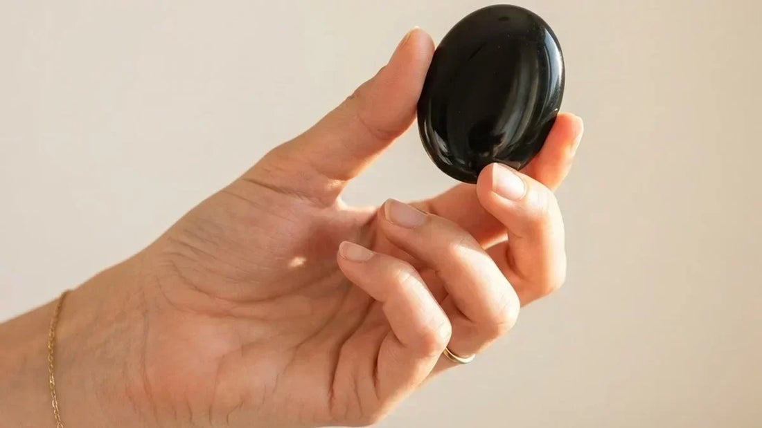 Piedra ónix negro pulido sostenida en la mano con luz natural, propiedades del ónix - Anna Piedra
