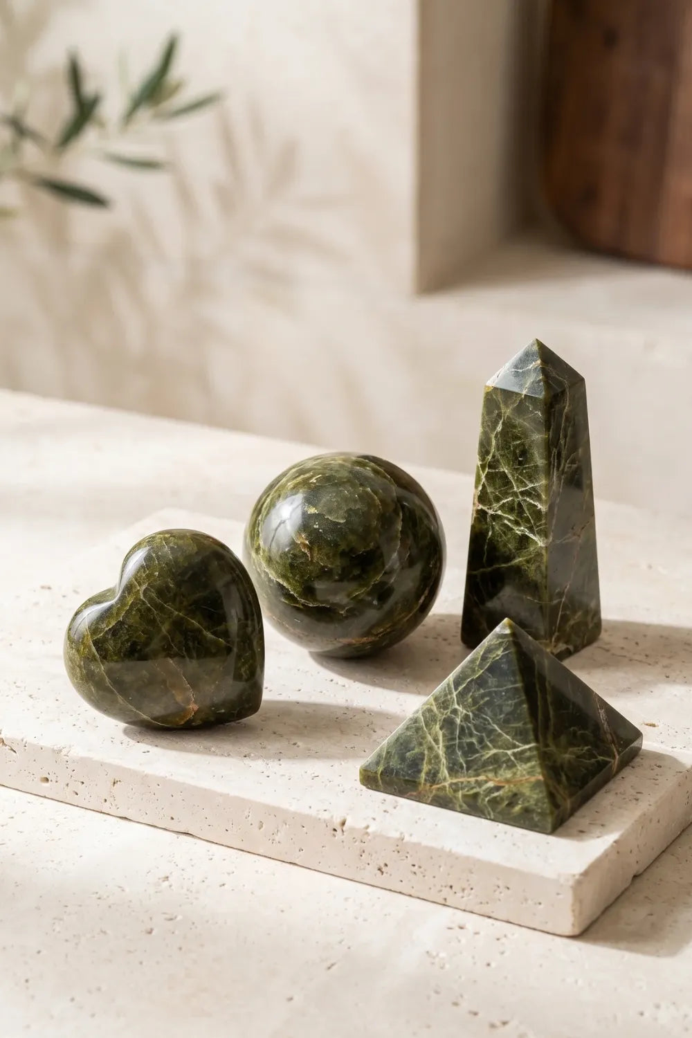 Set de epidota con corazón, esfera, obelisco y pirámide sobre una base de piedra en interior luminoso.
