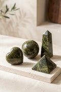 Set de epidota con corazón, esfera, obelisco y pirámide sobre una base de piedra en interior luminoso.