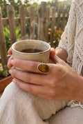 Mujer con anillo con ojo de tigre dorado sosteniendo una taza de café - Anna Piedra