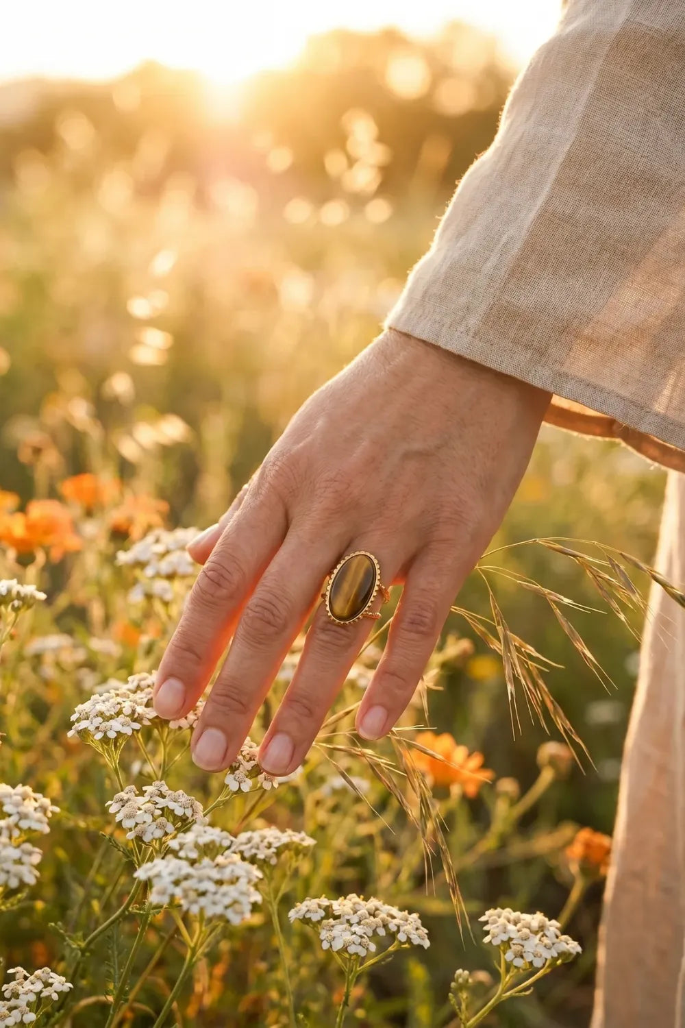 Mujer con anillo con ojo de tigre dorado entre flores silvestres a la luz del atardecer - Anna Piedra