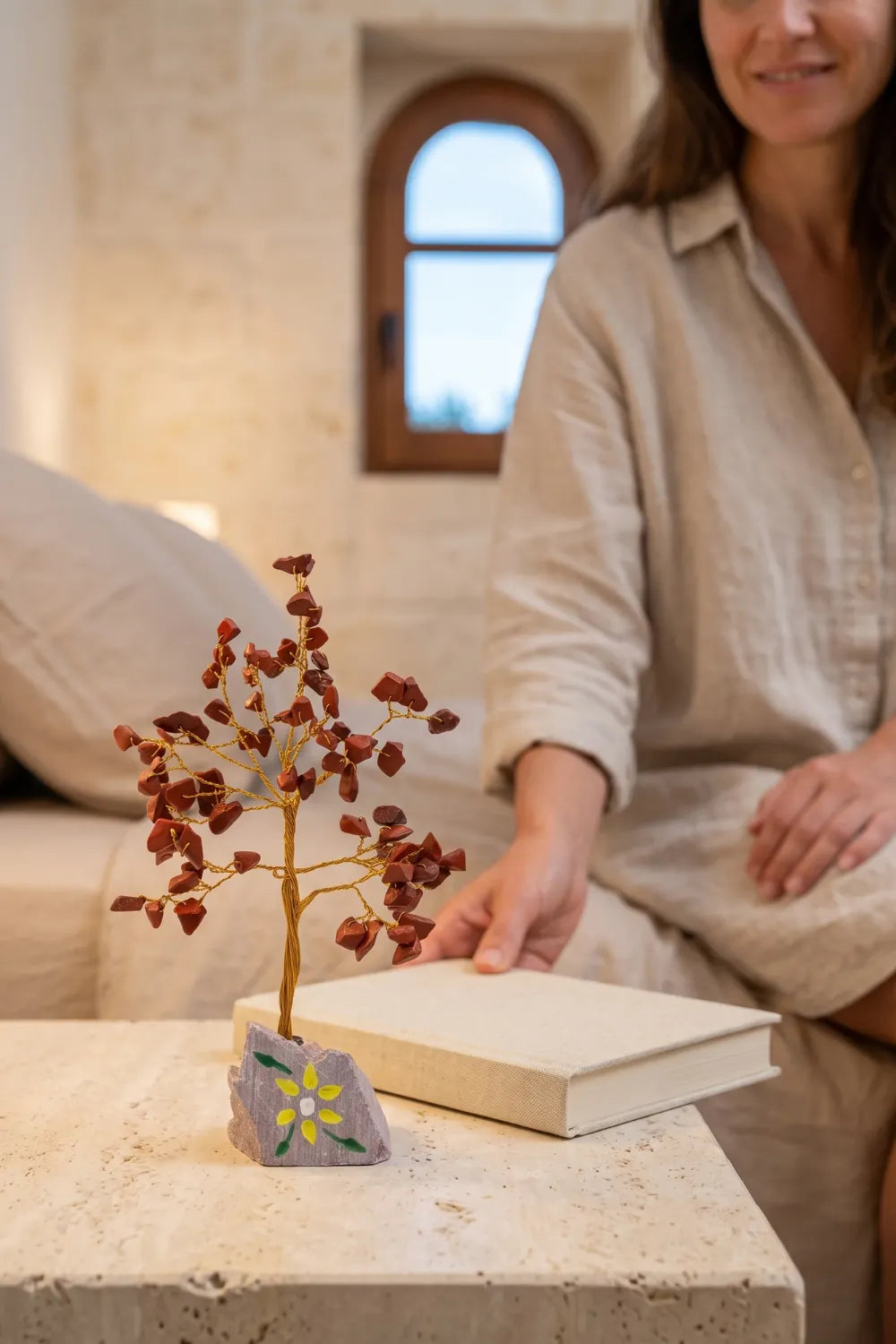 Árbol de la Vida de jaspe rojo decorativo sobre una mesa clara junto a un libro en un ambiente acogedor.