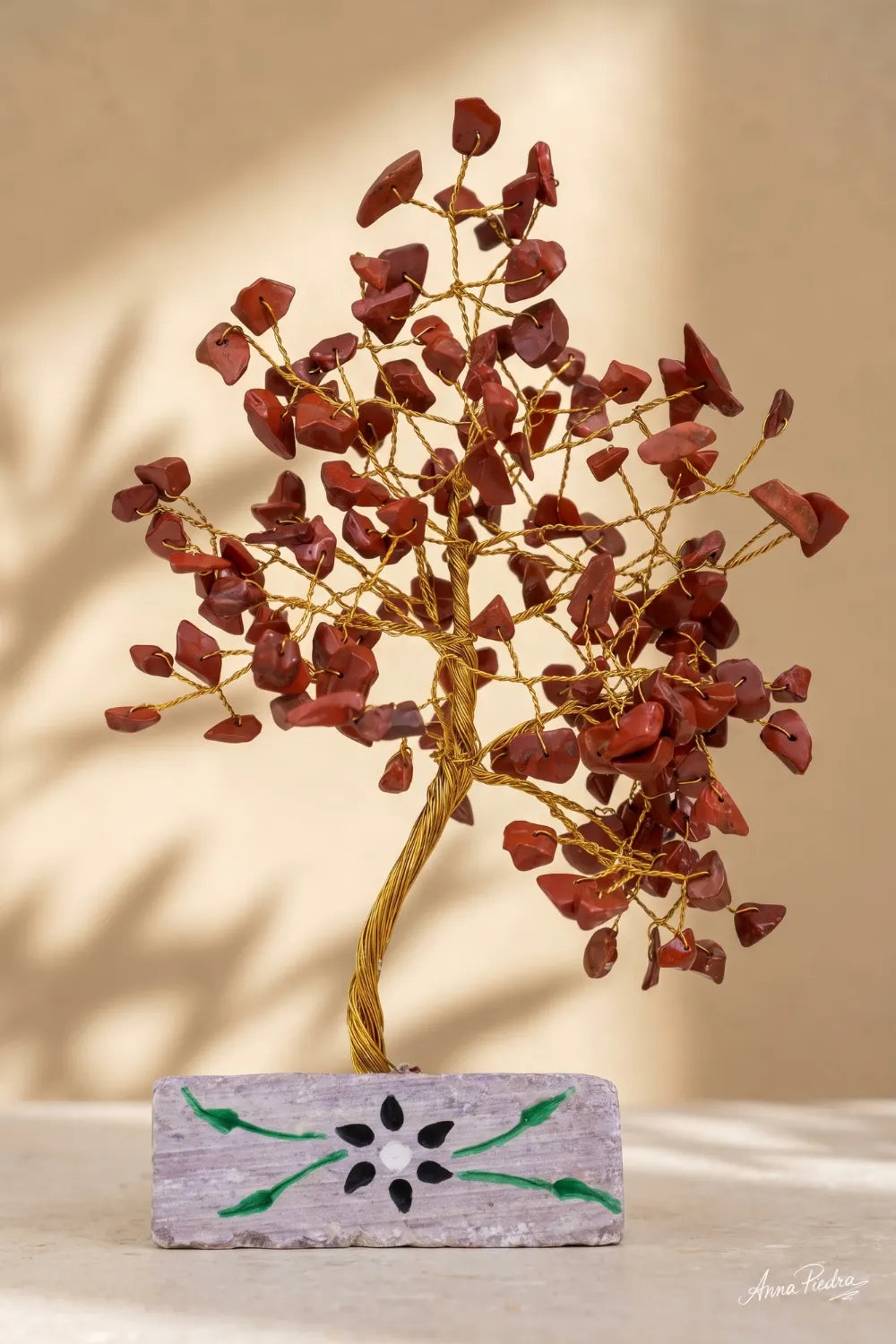 Árbol de la Vida de jaspe rojo con base decorativa, fotografiado sobre fondo cálido y minimalista.