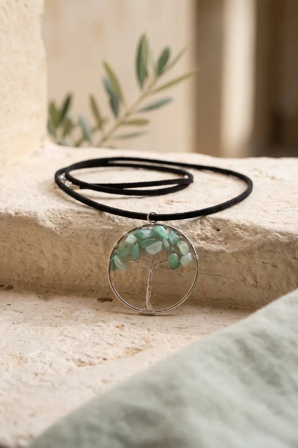 Colgante Árbol de la Vida de jade colocado sobre una superficie de piedra clara con cordón negro.