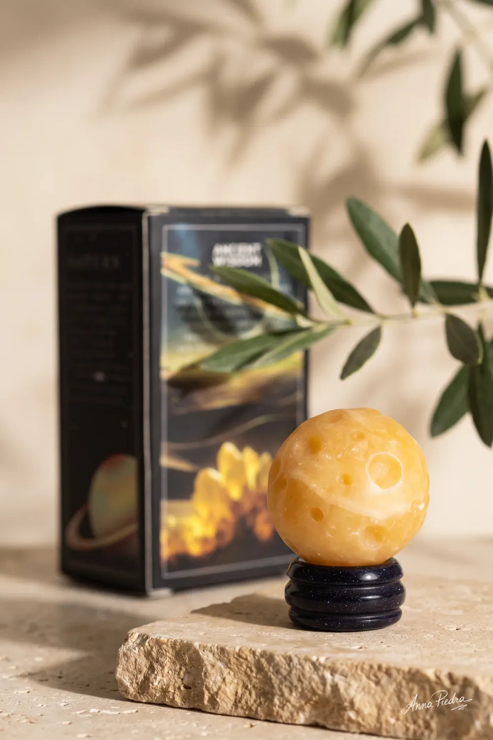 Esfera de jade amarillo Planeta Saturno sobre base oscura con su caja de presentación al fondo.
