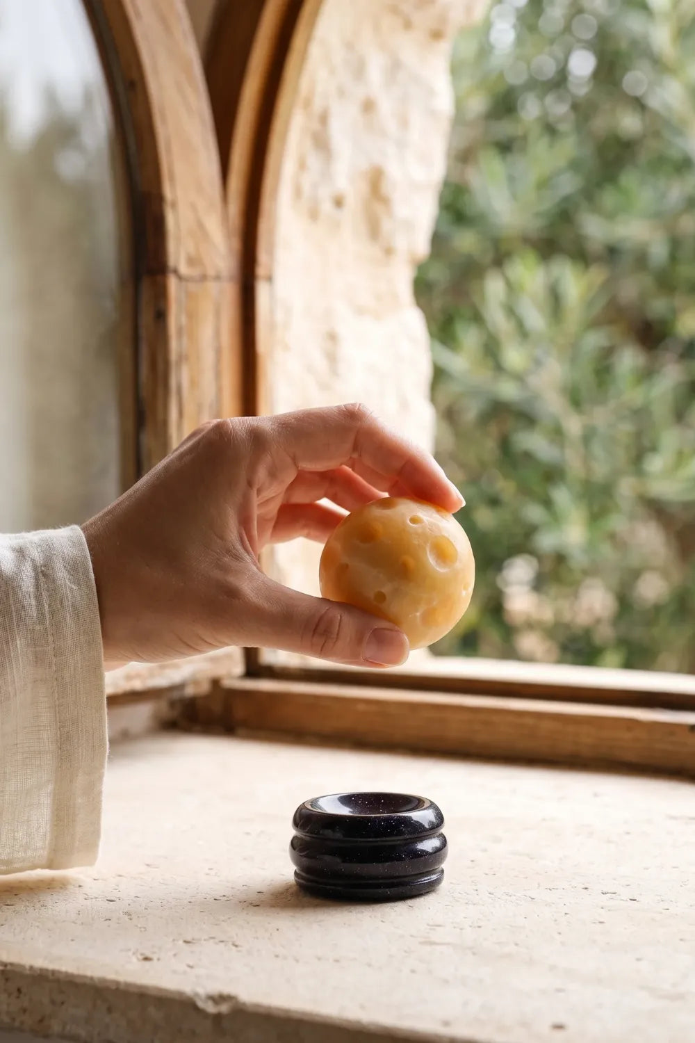 Mano sosteniendo una esfera de jade amarillo Planeta Saturno junto a su soporte oscuro.