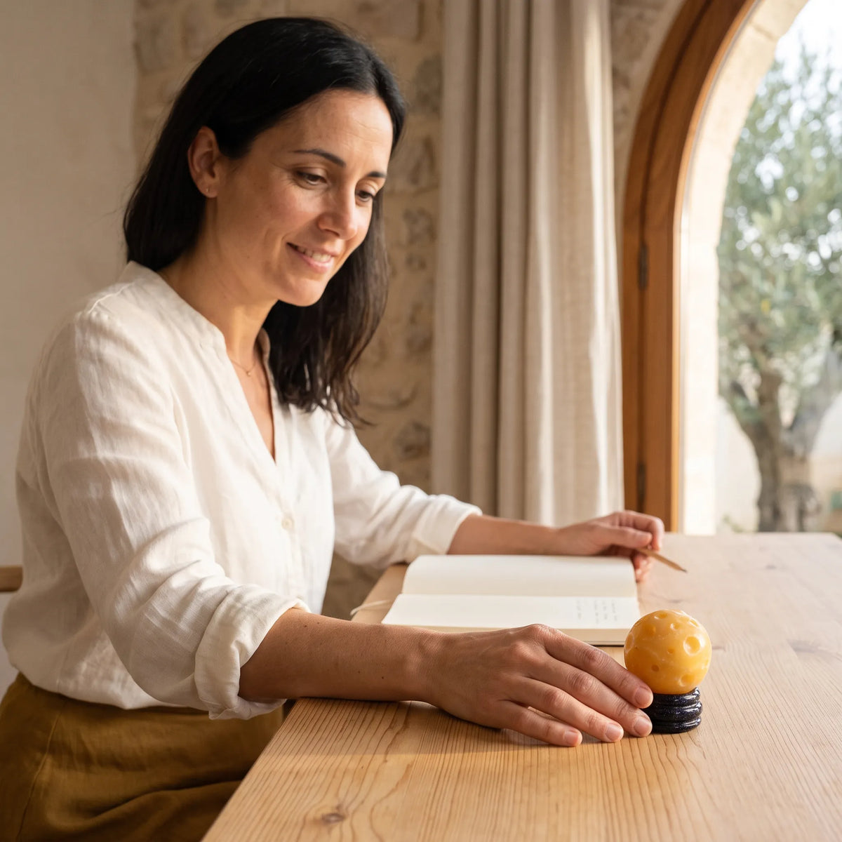 Mujer sentada junto a una ventana con una esfera de jade amarillo Planeta Saturno sobre la mesa.