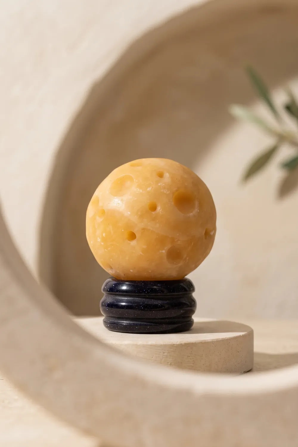 Esfera de jade amarillo Planeta Saturno expuesta sobre una base oscura en un nicho decorativo de piedra.