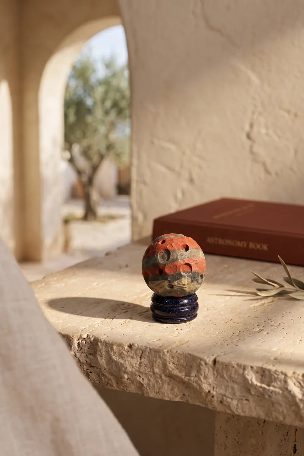 Planeta Marte de jaspe rojo sobre una superficie de piedra, con un libro decorativo en un ambiente mediterráneo.