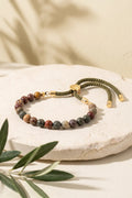 Pulsera de jaspe Picasso ajustable presentada sobre una base de piedra clara con ramas de olivo.