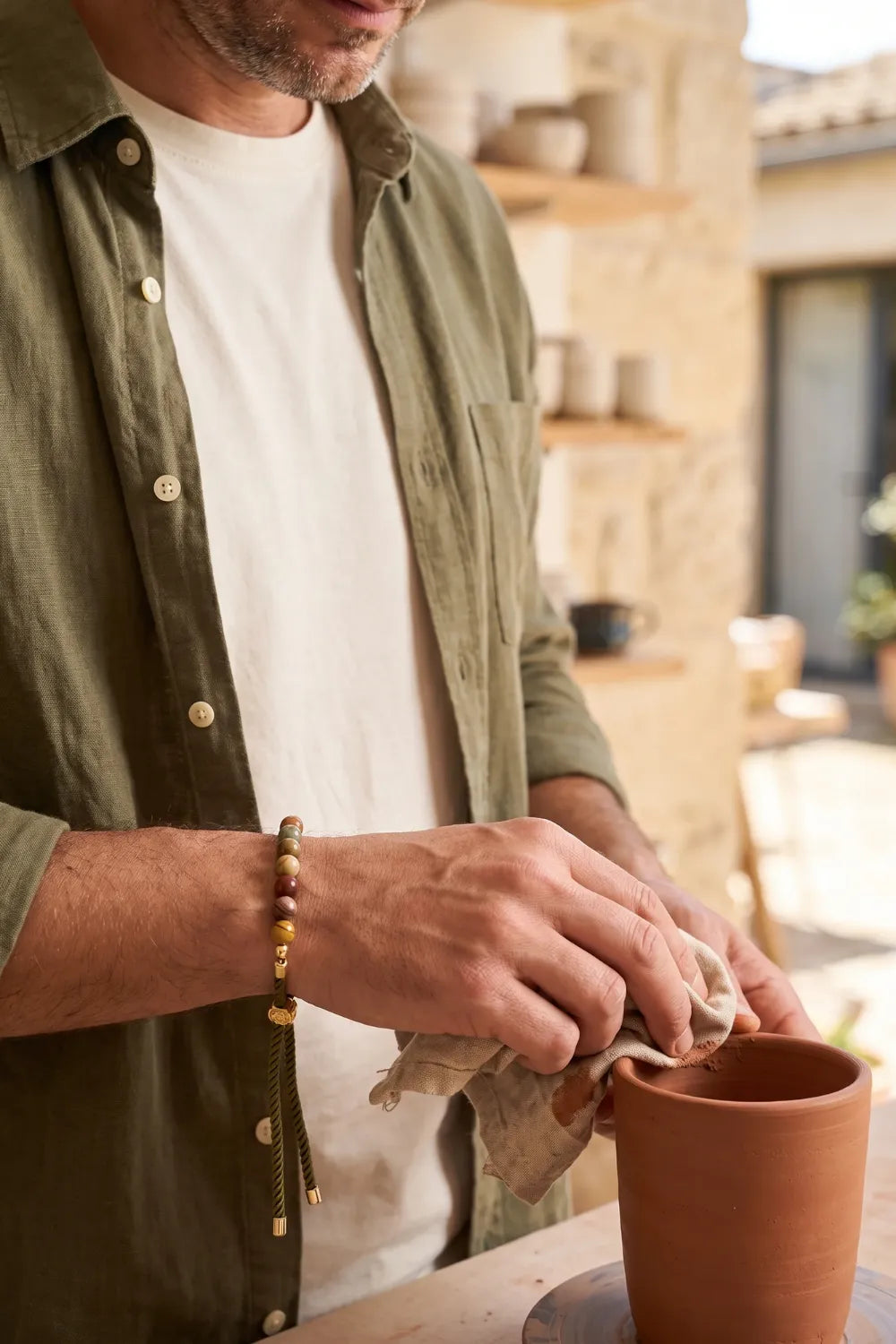 Hombre llevando una pulsera de jaspe Picasso ajustable mientras limpia una maceta de terracota.