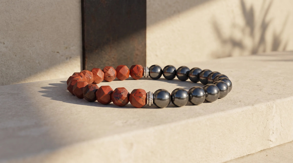 Pulsera de jaspe rojo y hematita magnética colocada sobre una superficie de piedra clara con luz natural.
