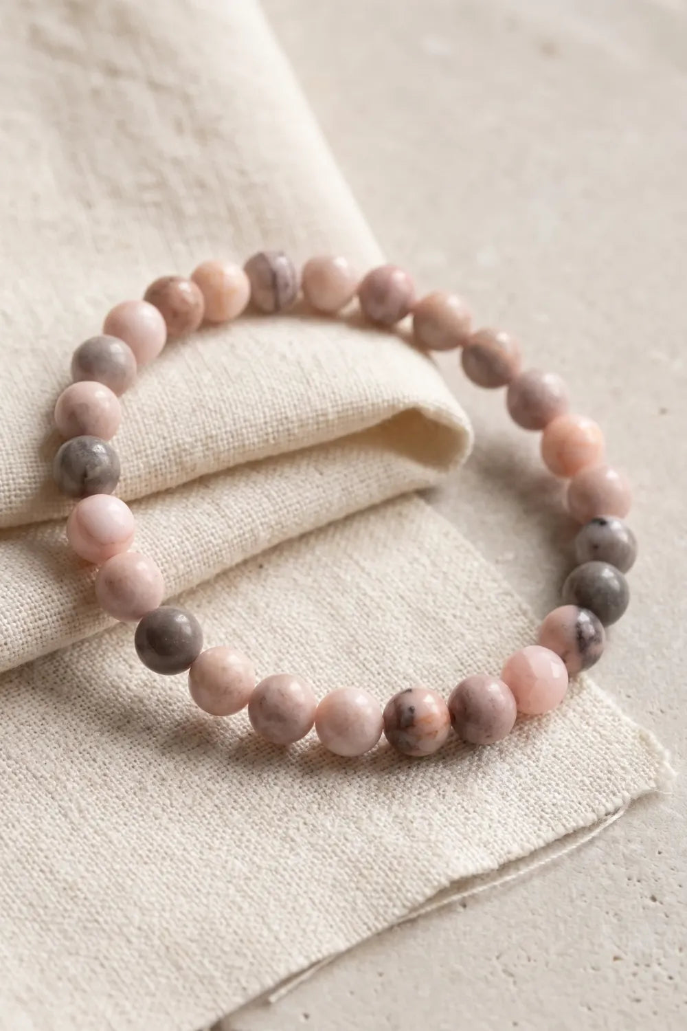 Detalle de una pulsera de jaspe rosa con cuentas redondas sobre tela de lino clara.