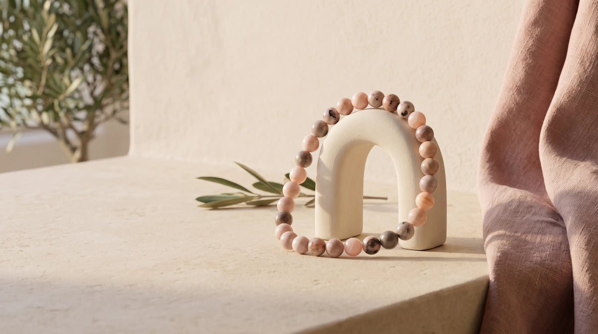 Pulsera de jaspe rosa colocada sobre un expositor en forma de arco en un ambiente cálido y natural.
