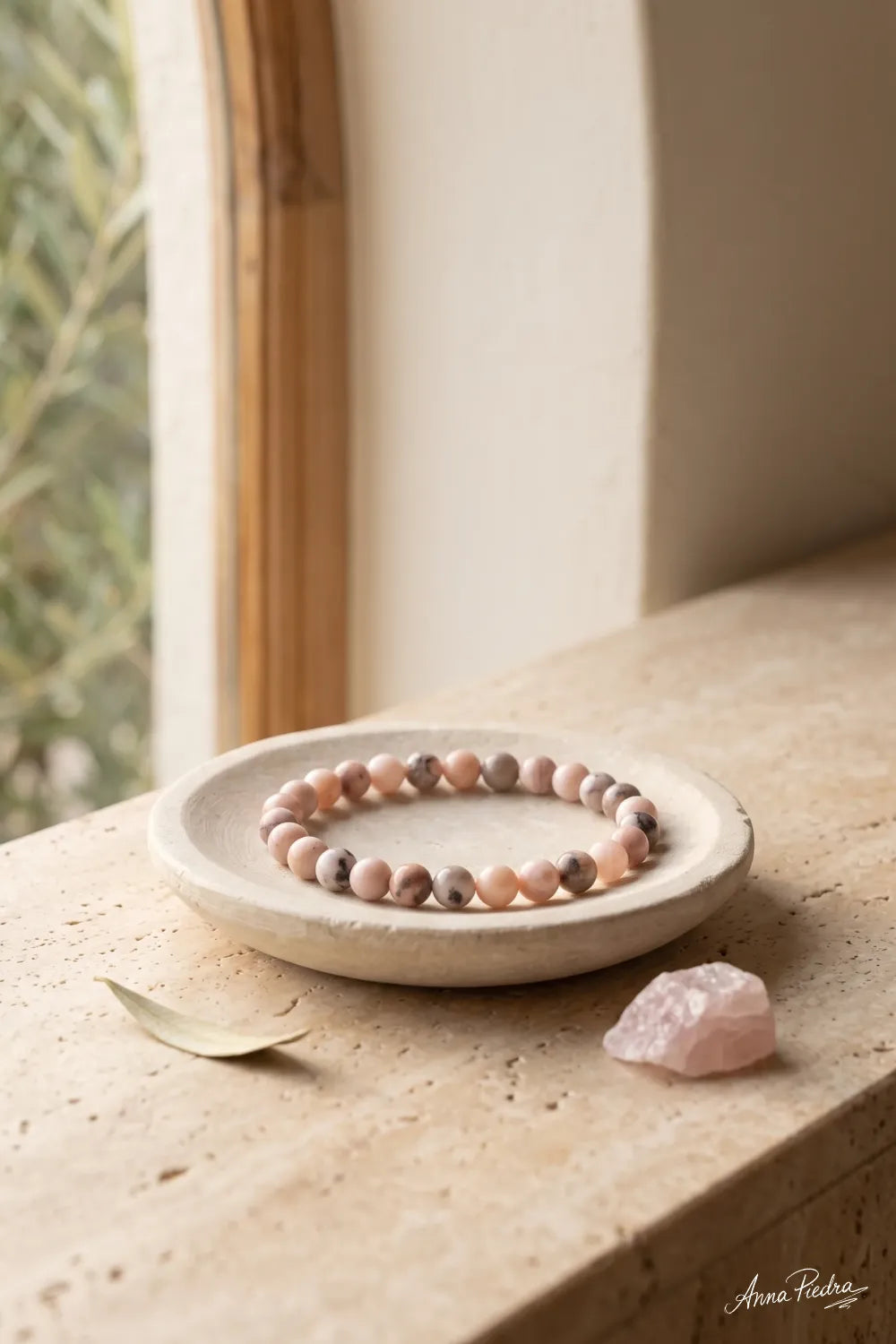 Pulsera de jaspe rosa presentada sobre un plato de cerámica junto a una piedra rosa en un interior sereno.