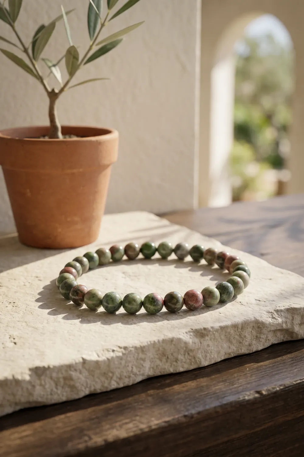 Pulsera de jaspe verde colocada sobre una piedra clara junto a una maceta de barro.