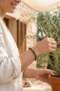 Mujer llevando una pulsera de jaspe verde mientras cuida una planta de romero.