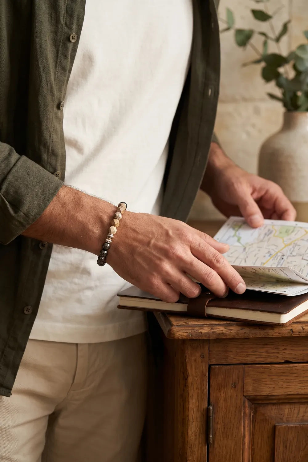 Hombre con pulsera de jaspe paisaje y hematita magnética en la muñeca mientras consulta un mapa sobre una mesa de madera.