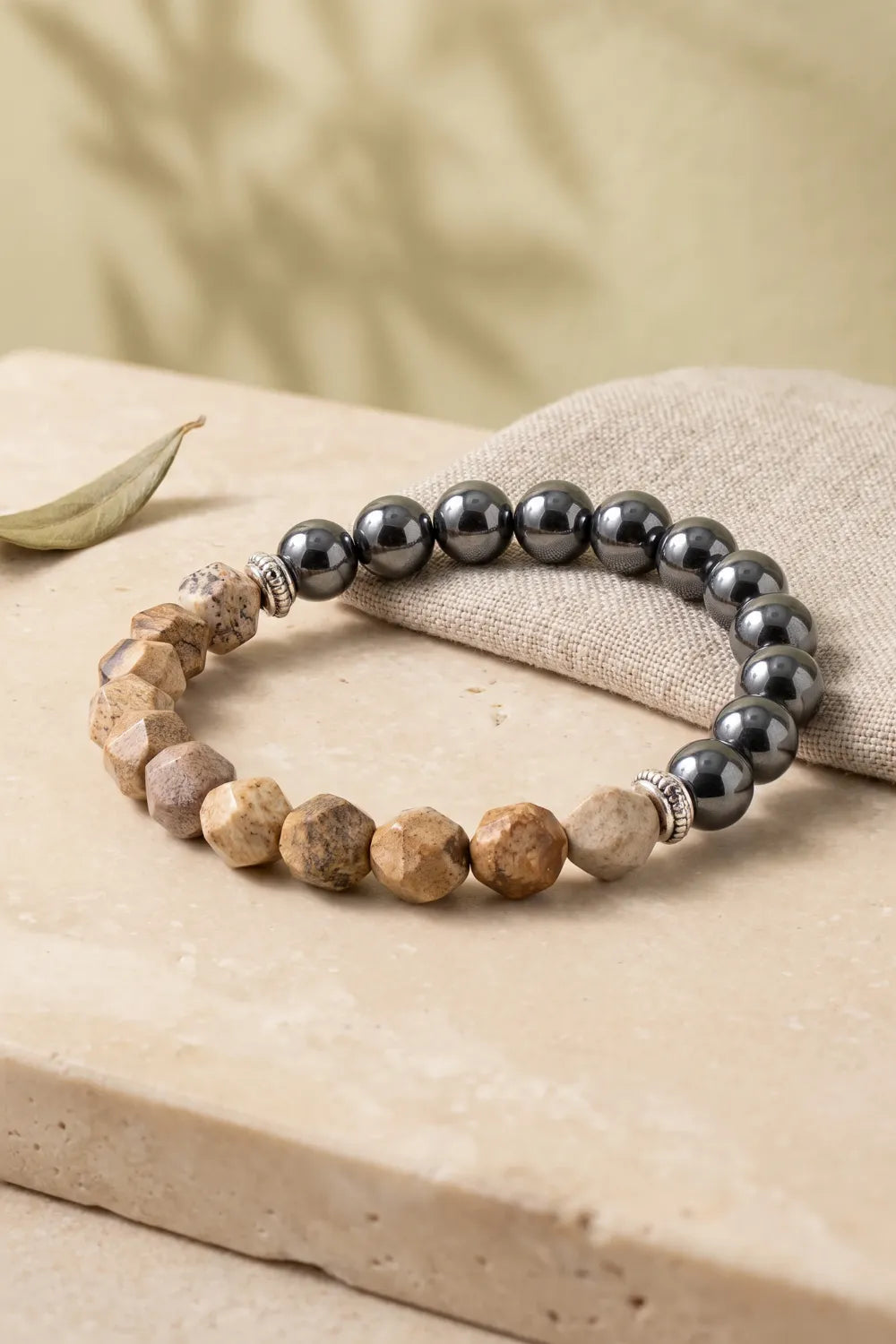 Pulsera de jaspe paisaje y hematita magnética con separadores plateados sobre lino beige y piedra natural.