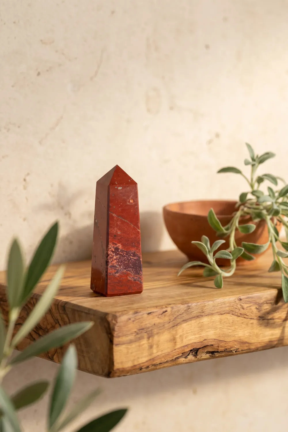 Punta de jaspe rojo sobre una balda de madera con decoración natural y hojas de olivo en un ambiente mediterráneo.