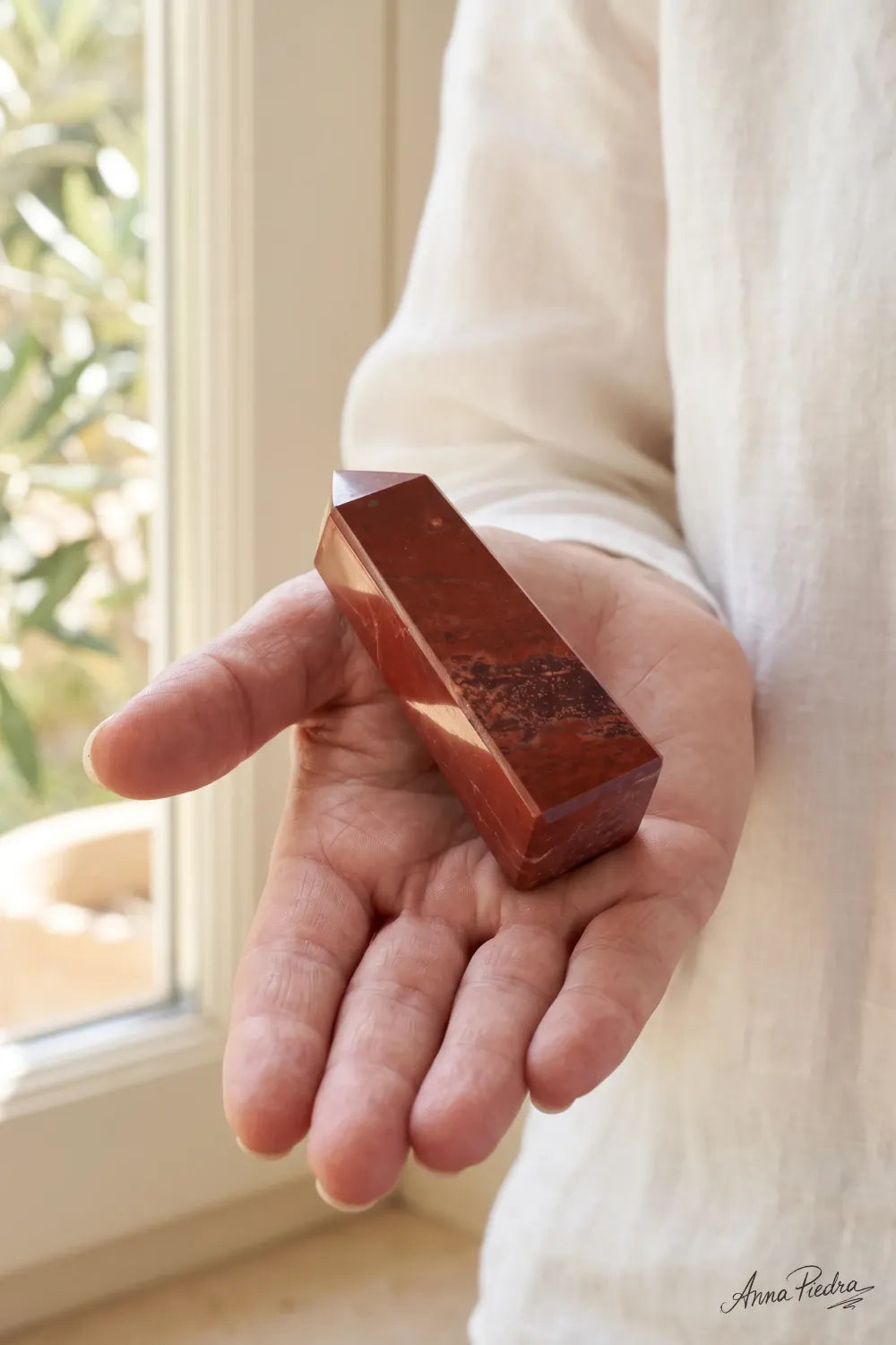 Mujer sosteniendo una punta de jaspe rojo pulida en la mano junto a una ventana con luz natural.