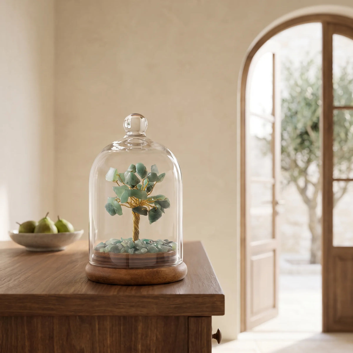 Árbol de la Vida de Aventurina verde bajo cúpula de vidrio con base de madera, sobre un mueble de madera en un interior mediterráneo – Anna Piedra