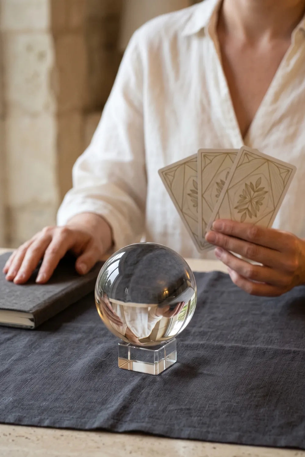 Bola de cristal transparente para adivinación sobre soporte junto a una mujer que sostiene cartas.