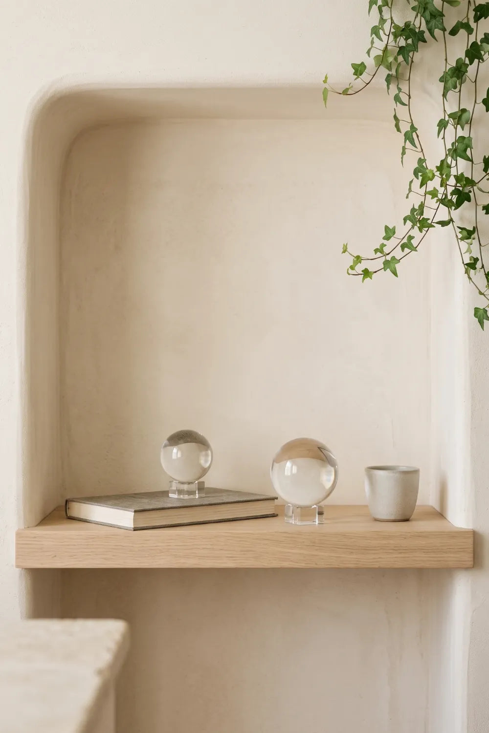 Dos bolas de cristal decorativas transparentes de diferentes tamaños en una estantería de madera con libro y cerámica – Anna Piedra.