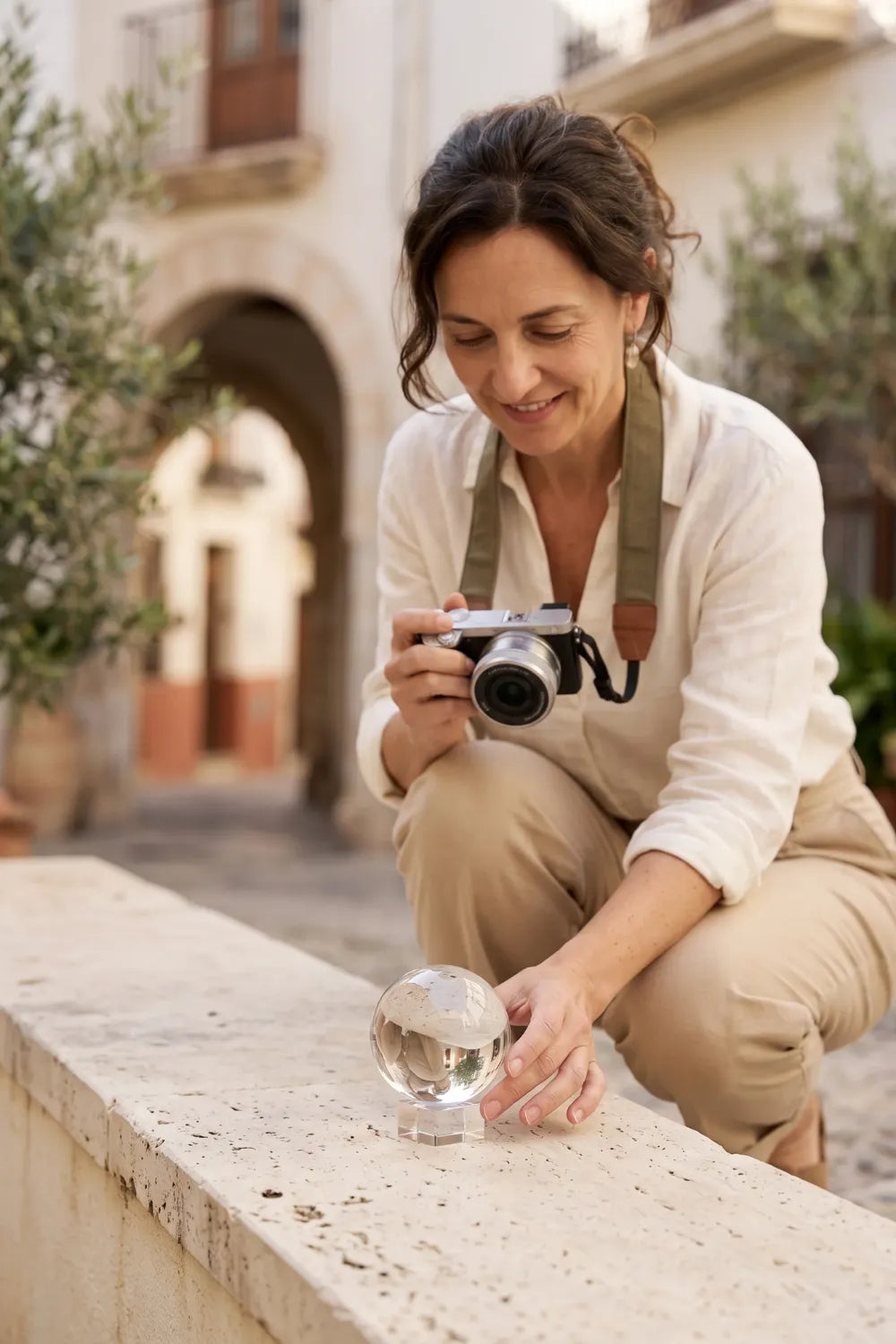 Mujer preparando una fotografía con bola de cristal transparente y cámara en una calle de piedra.