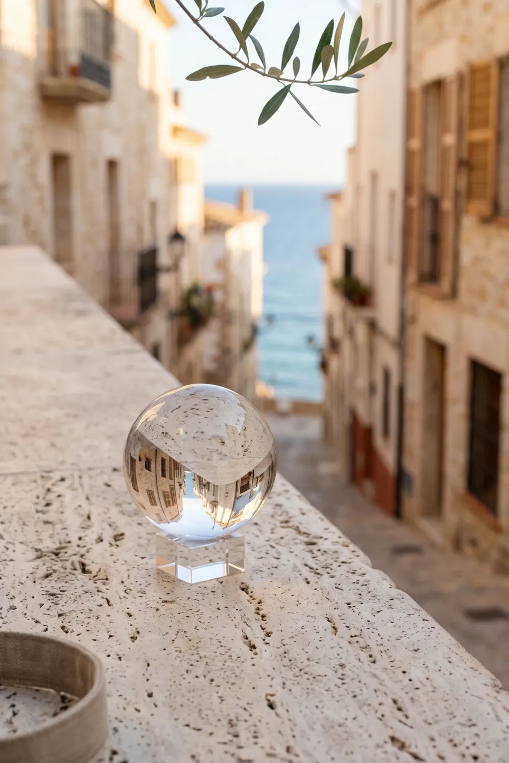 Bola de cristal para fotografía sobre una barandilla de piedra con reflejo invertido de una calle mediterránea junto al mar.