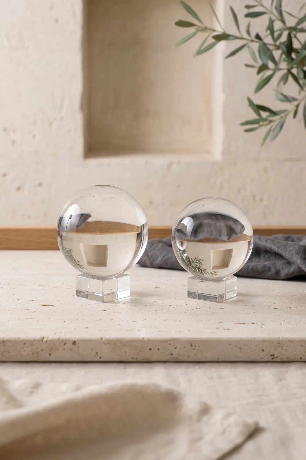 Dos bolas de cristal transparentes de diferentes tamaños sobre soportes cuadrados en una superficie de piedra.