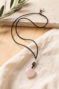 Colgante de cuarzo rosa en forma de corazón con cordón negro ajustable, sobre tela de lino beige y madera natural – Anna Piedra
 Copier