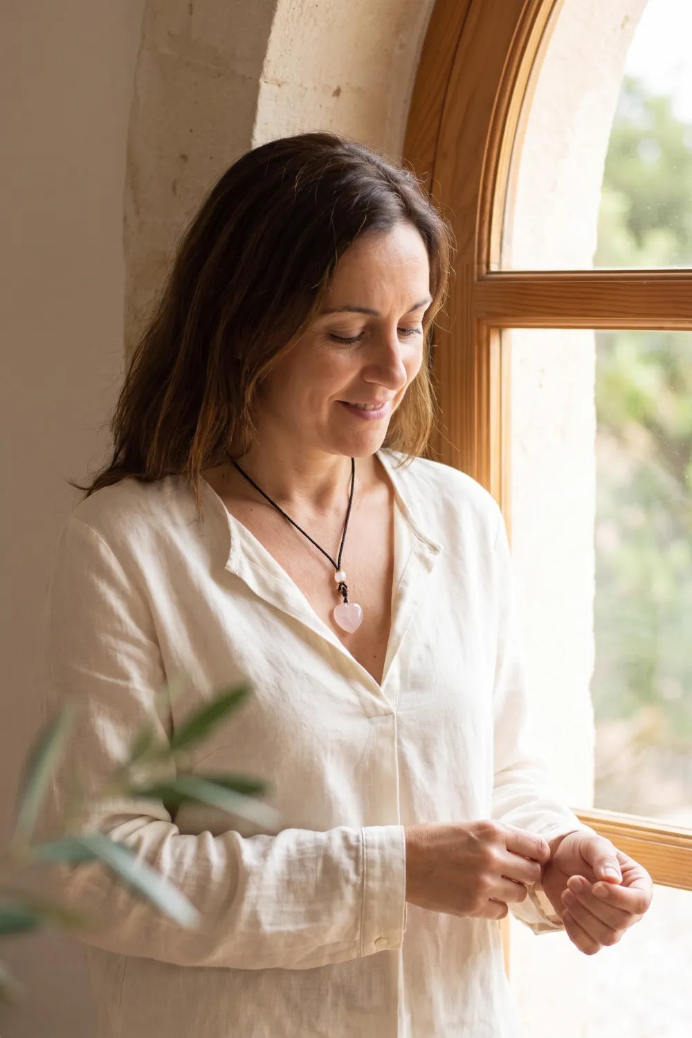 Mujer llevando un colgante de cuarzo rosa en forma de corazón con cordón negro sobre una blusa blanca junto a una ventana – Anna Piedra
 Copier