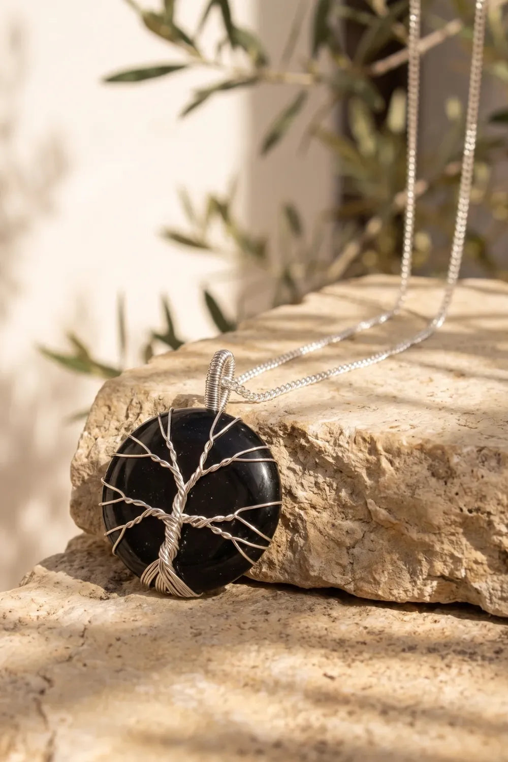 Collar árbol de la vida de ónix negro apoyado sobre una piedra clara en un entorno mediterráneo. anna piedra