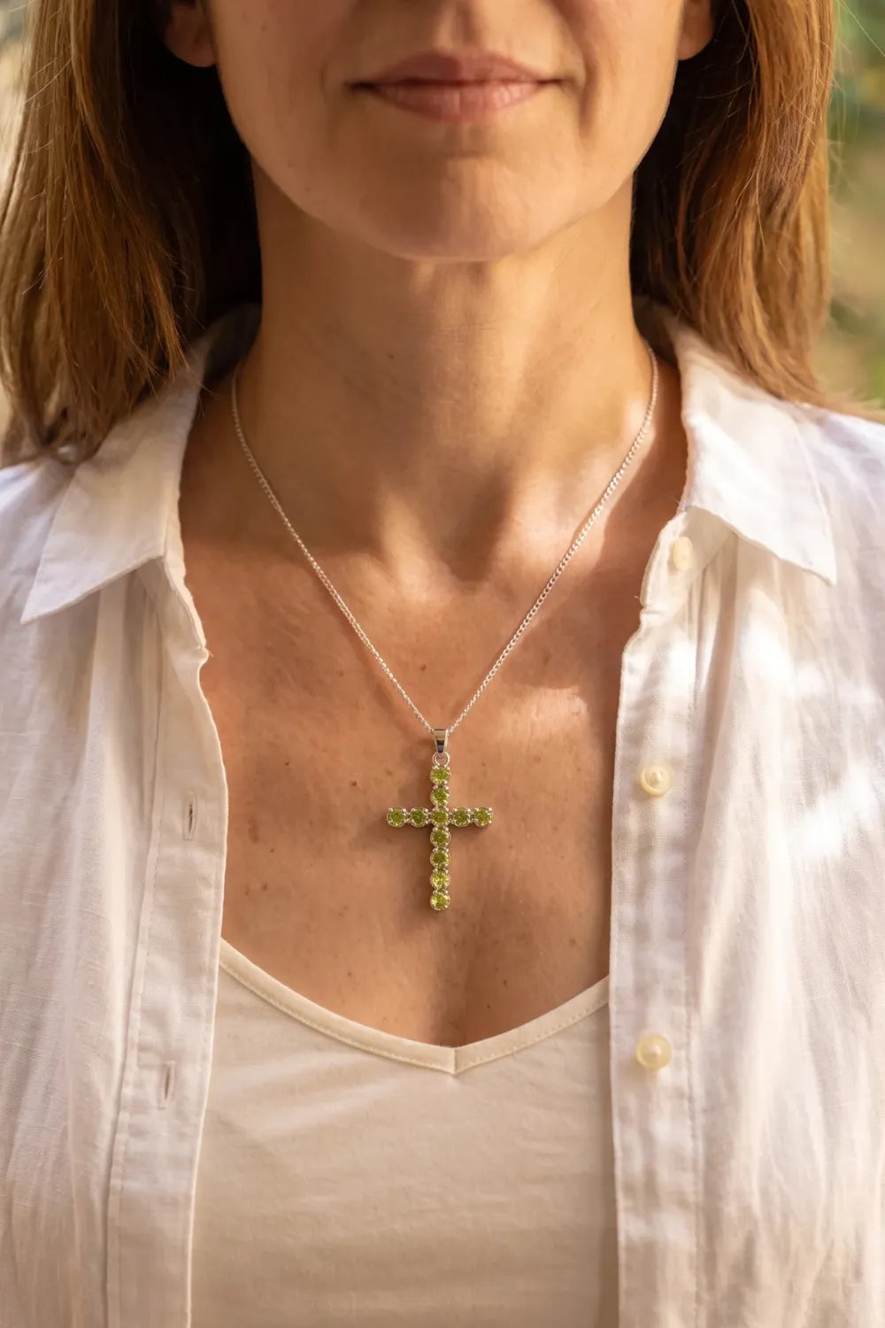 Detalle de collar crucifijo de peridoto natural con cadena plateada sobre el pecho de una mujer.