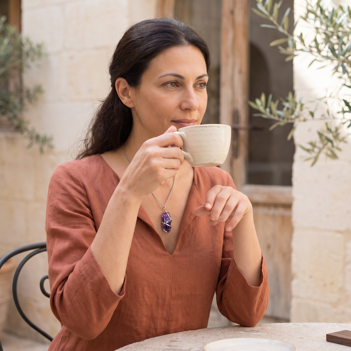 Mujer con collar de amatista en bruto de color violeta y cadena plateada, tomando café en una terraza mediterránea – Anna Piedra