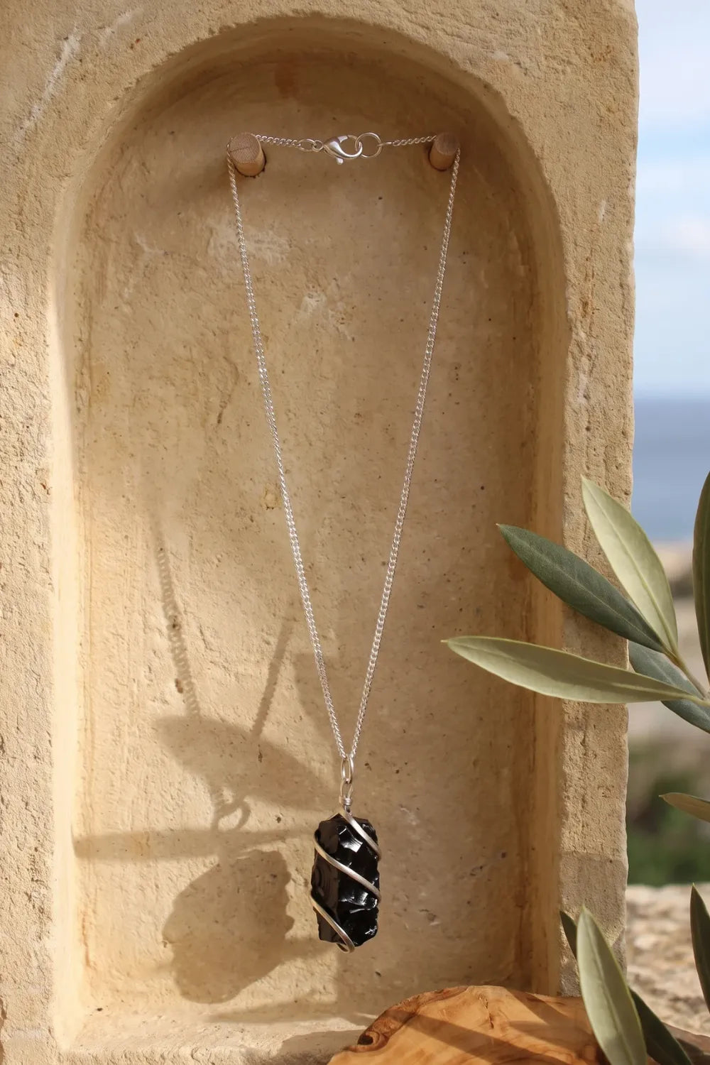 Collar de ónix negro en bruto con cadena plateada colgado en un nicho de piedra clara. anna piedra