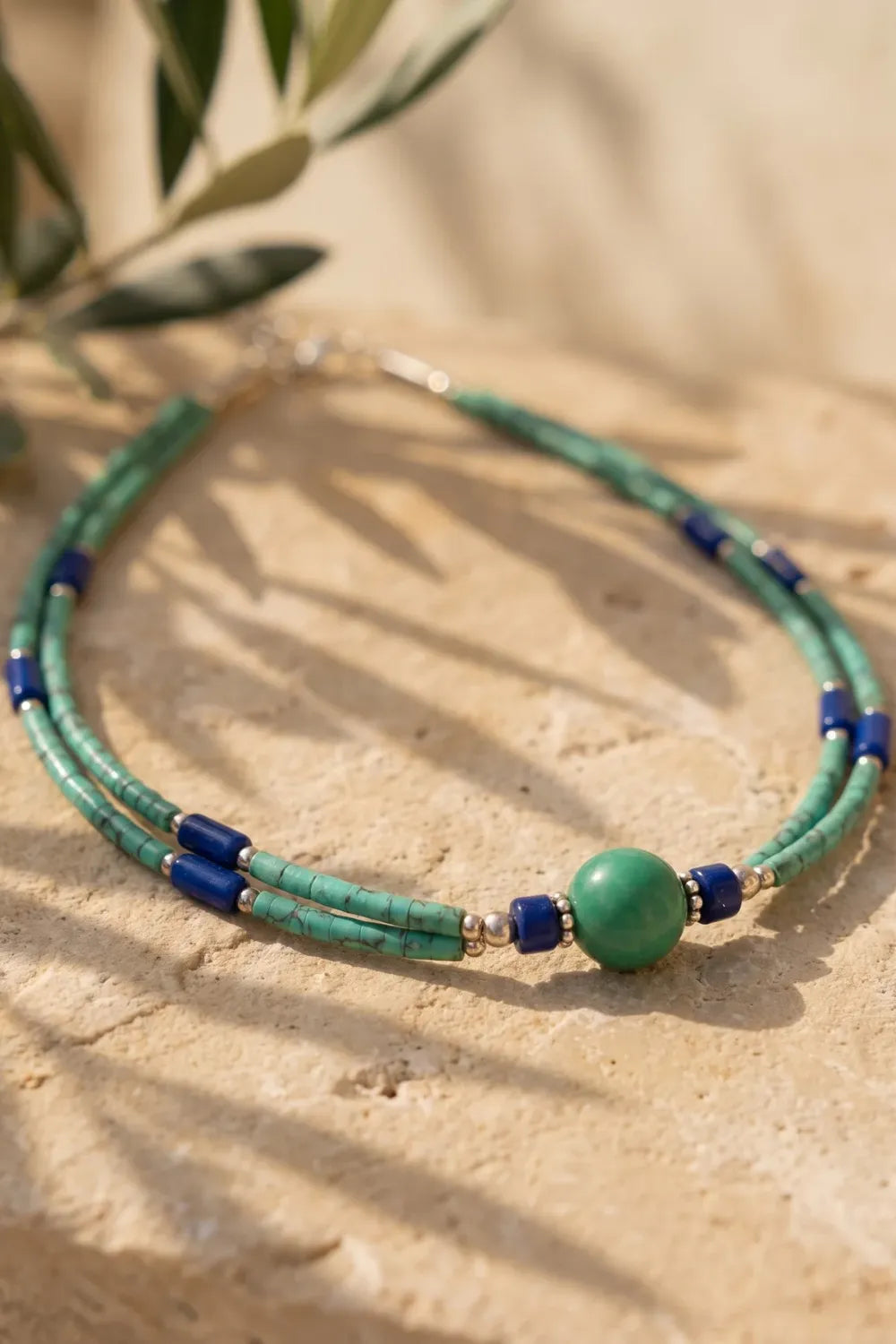 Detalle del collar de dos líneas con lapislázuli y malaquita sobre superficie de piedra clara - Anna Piedra