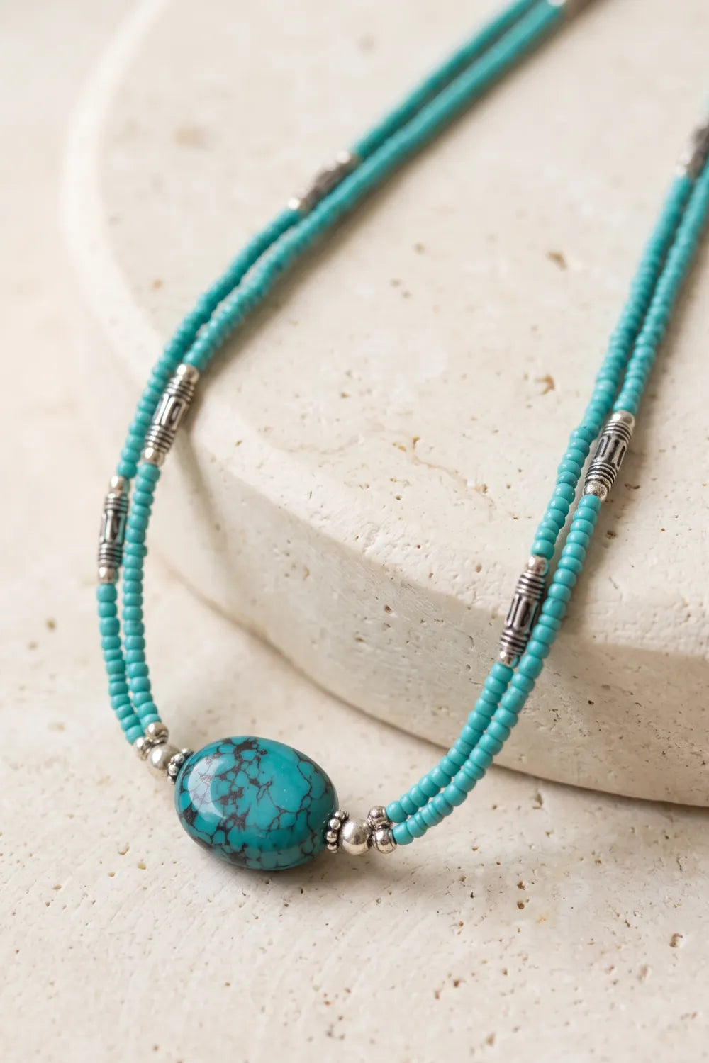 Primer plano del collar de turquesa de dos vueltas con piedra central azul de vetas oscuras, cuentas pequeñas y separadores plateados.