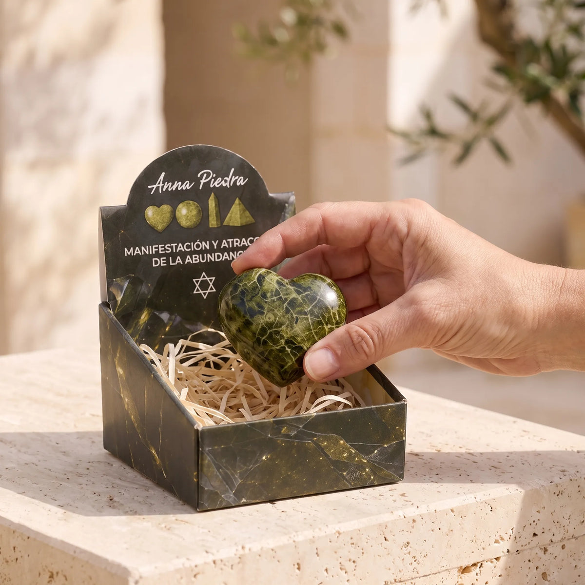 Corazón de epidota natural sostenido sobre su caja Anna Piedra con presentación artesanal.