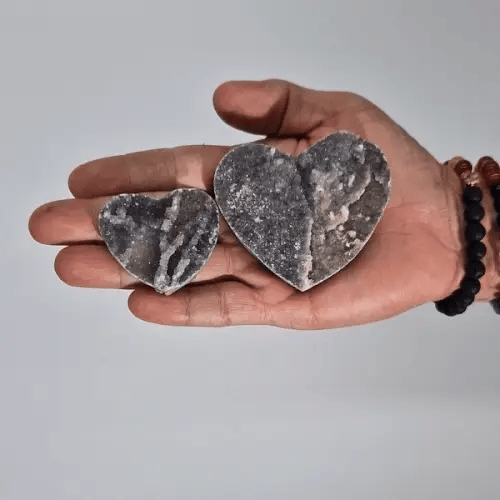 Dos corazones de calcita negra de distintos tamaños sostenidos sobre la palma de una mano. anna piedra