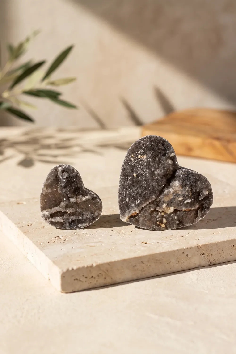Dos corazones de calcita negra de distintos tamaños sobre una base de piedra clara con luz natural. anna piedra