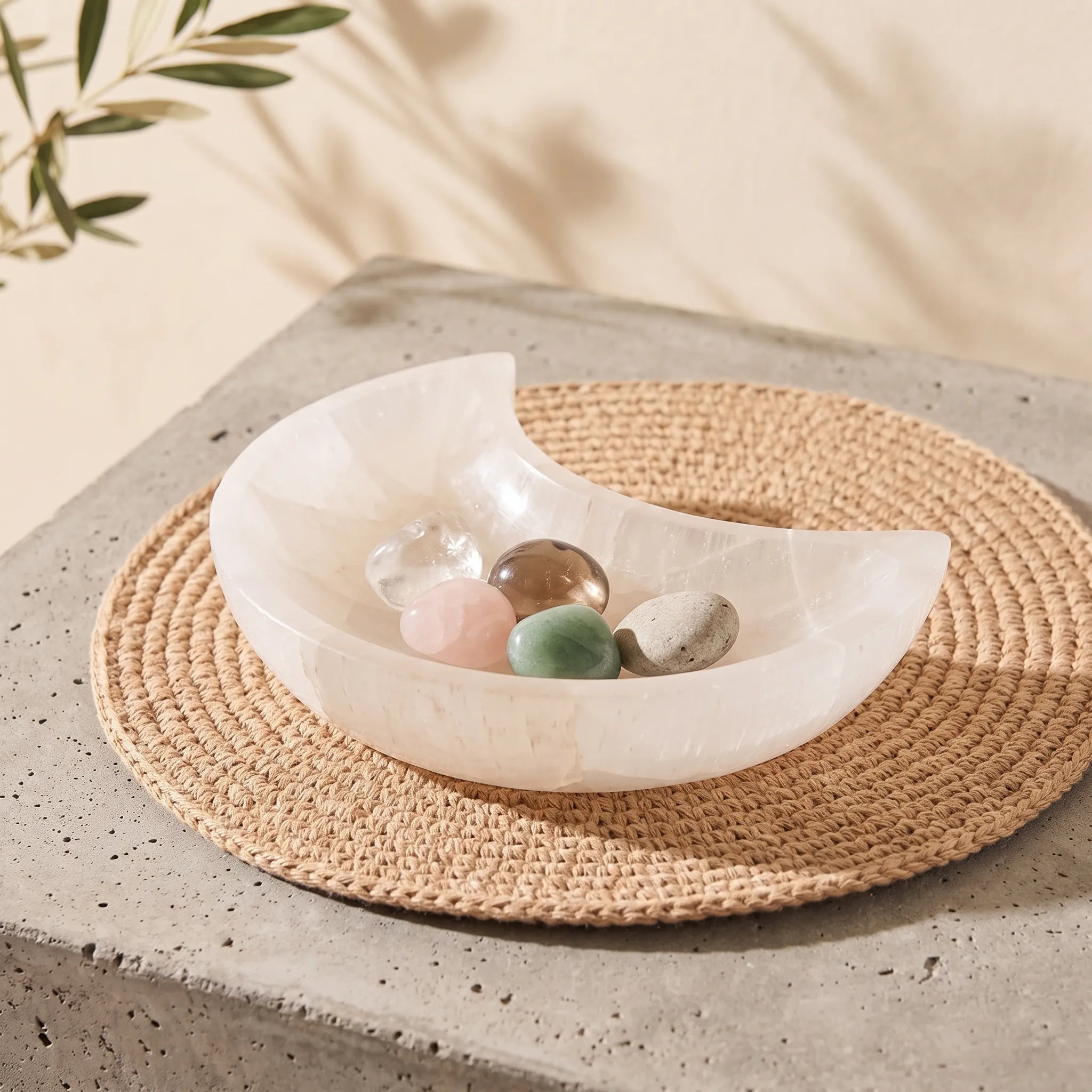 Cuenco de selenita luna con piedras naturales de colores en su interior sobre mesa de piedra - Anna Piedra