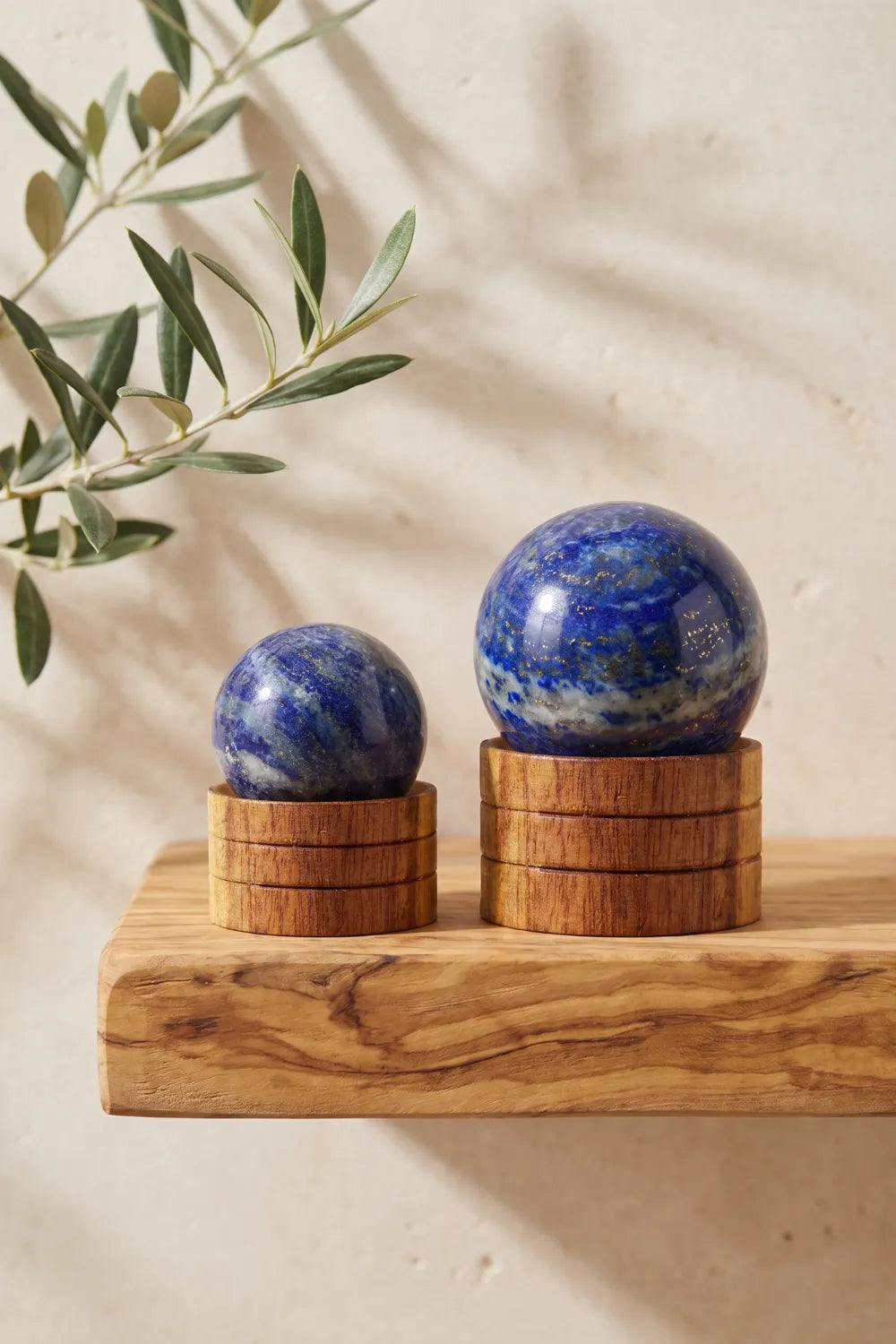 Dos esferas de lapislázuli sobre bases de madera colocadas en una balda de madera con rama de olivo