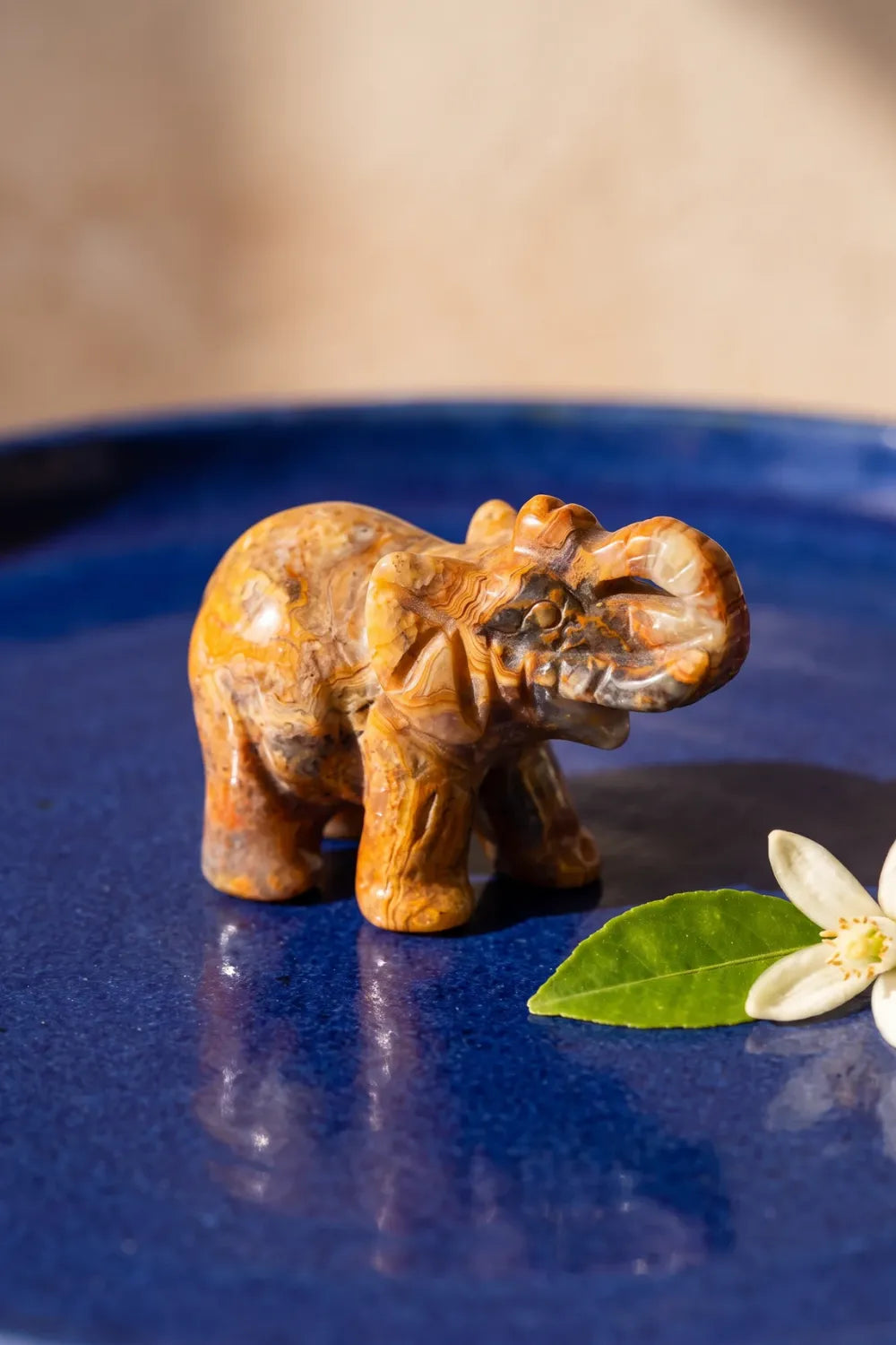 Elefante de la suerte tallado en ágata encaje loco sobre un plato azul, junto a una flor de azahar - Anna Piedra
