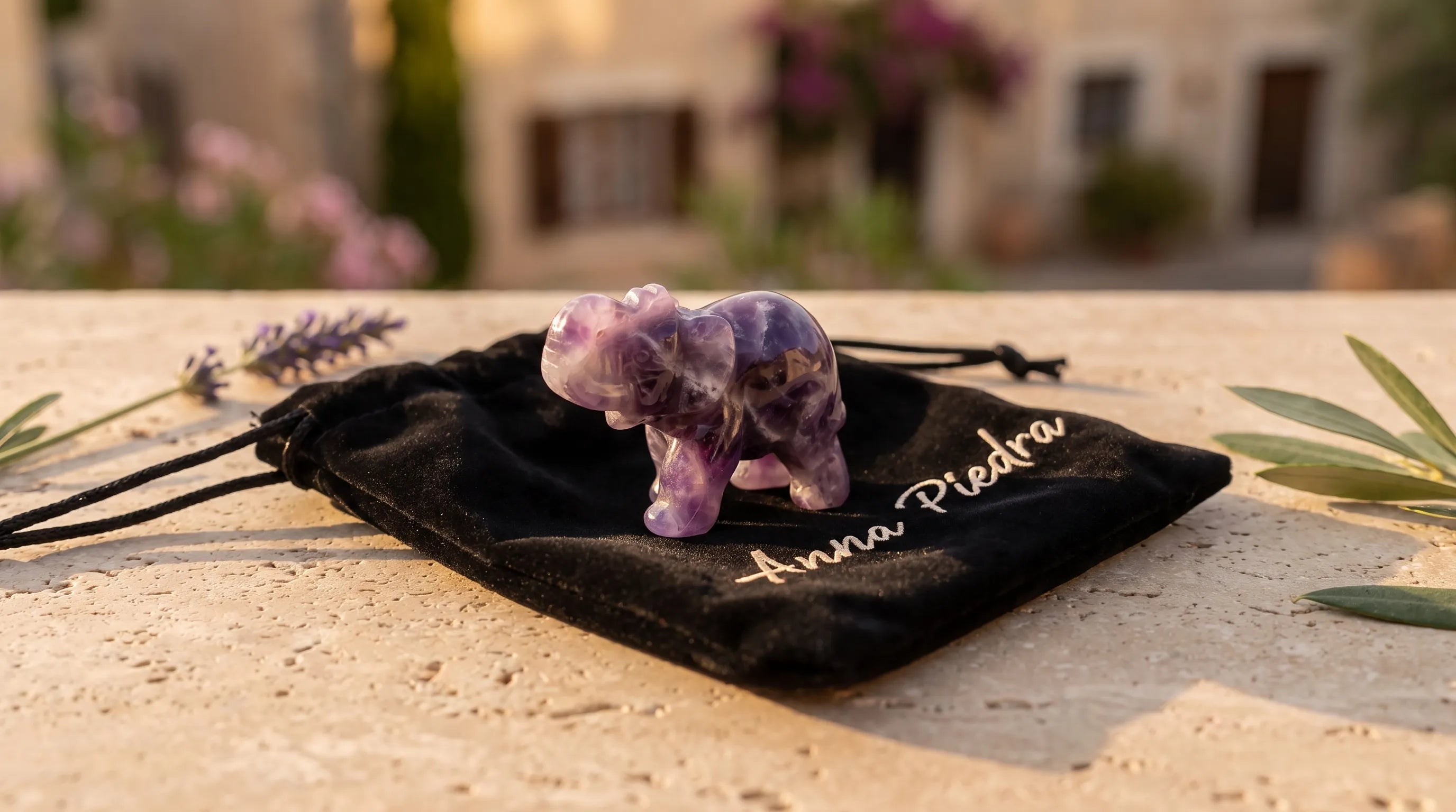 Elefante de la suerte tallado en amatista sobre una bolsa de terciopelo Anna Piedra, en una terraza con lavanda - Anna Piedra