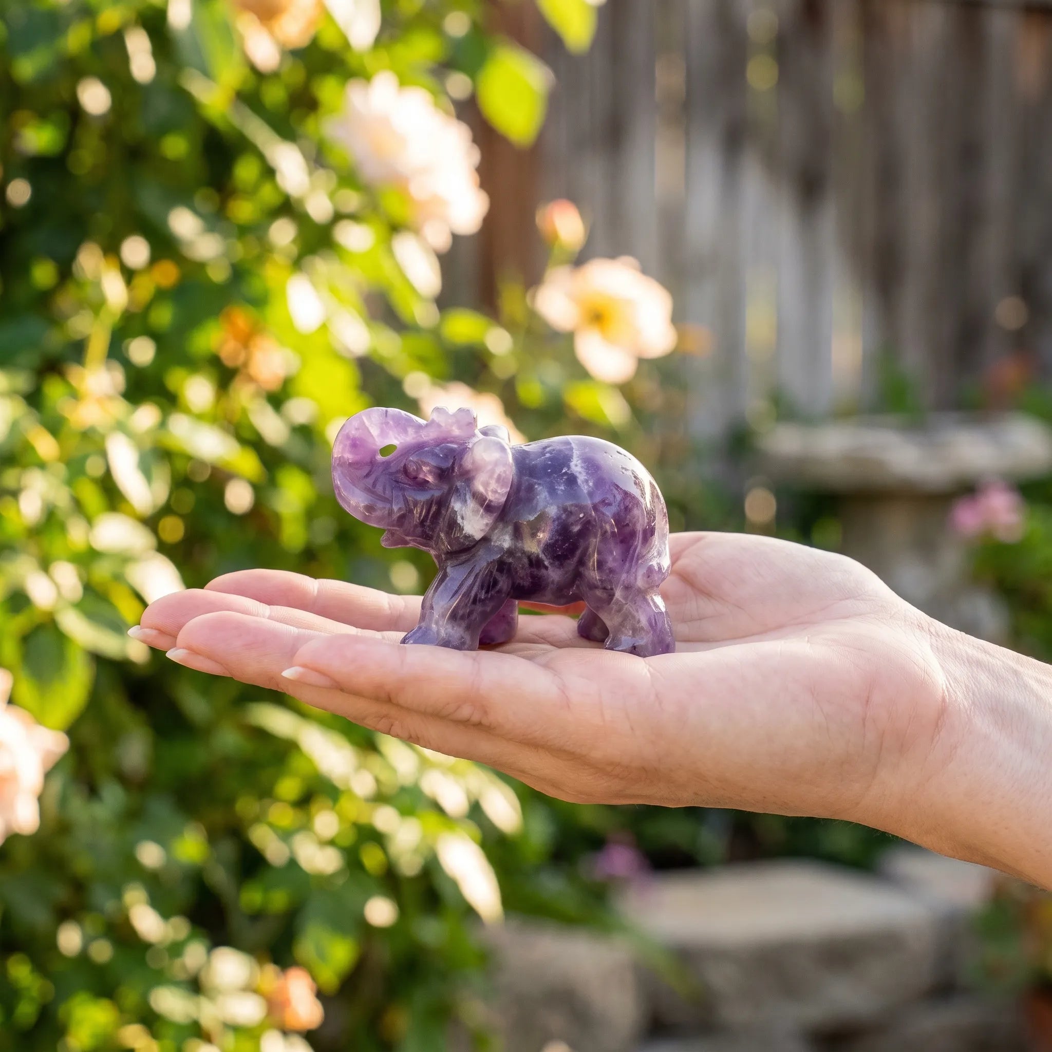 Figura de elefante de la suerte tallada en amatista sobre la palma de una mano, en un jardín - Anna Piedra