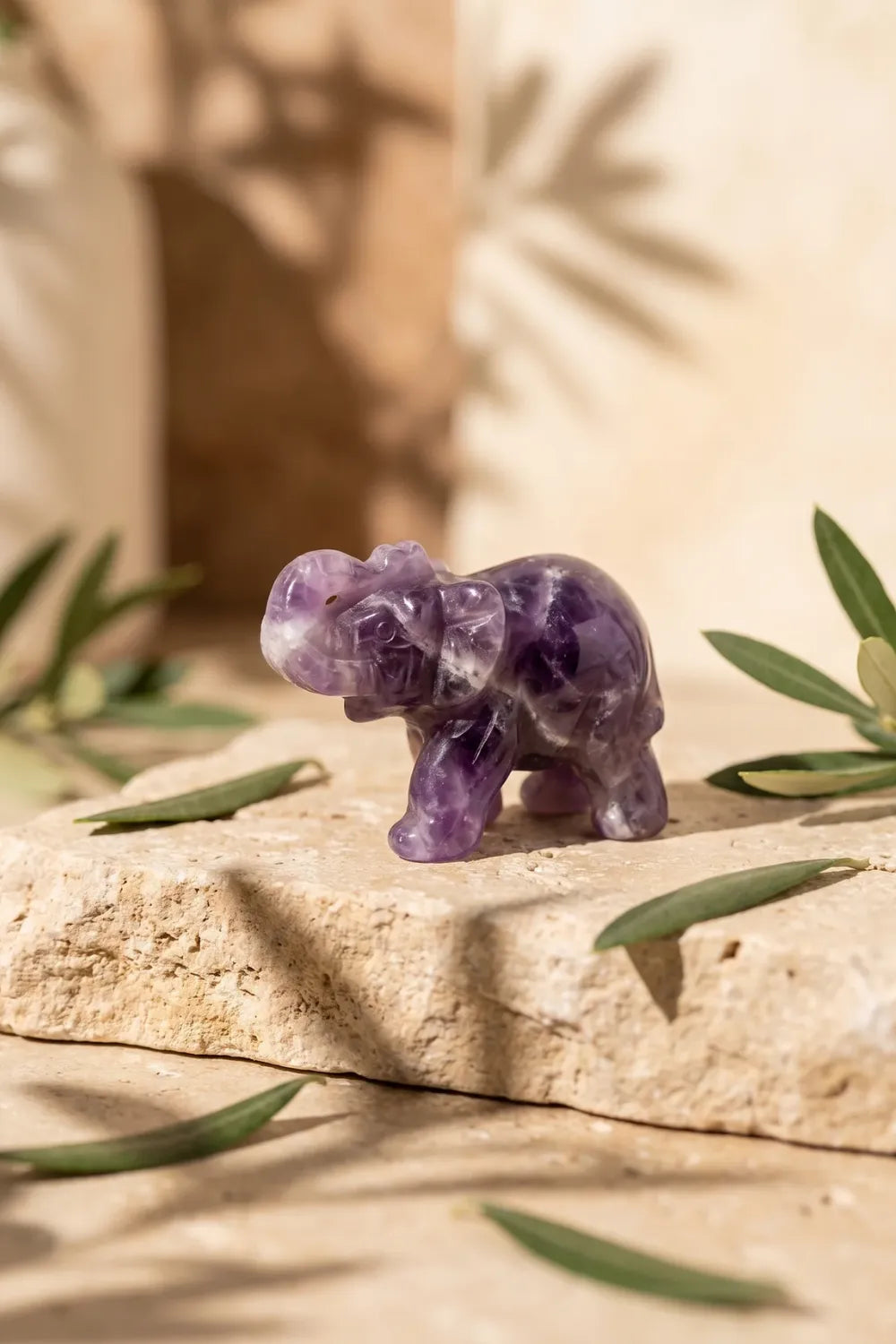 Elefante de la suerte tallado en amatista sobre una piedra de travertino en un jardín - Anna Piedra