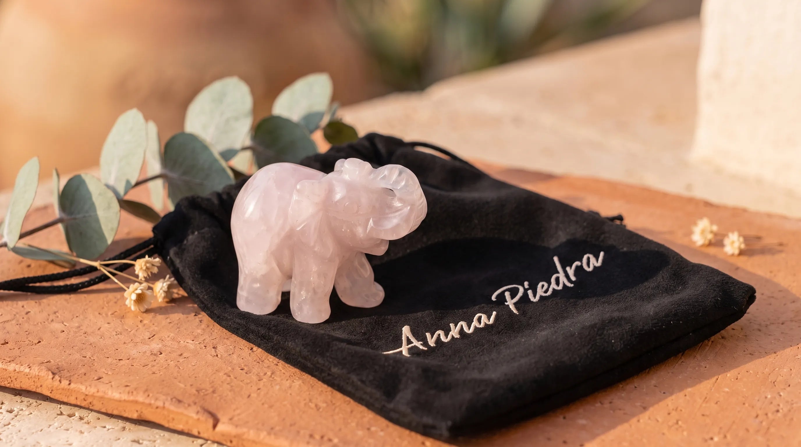 Elefante de la suerte tallado en cuarzo rosa sobre una bolsa de terciopelo Anna Piedra, junto a eucalipto - Anna Piedra