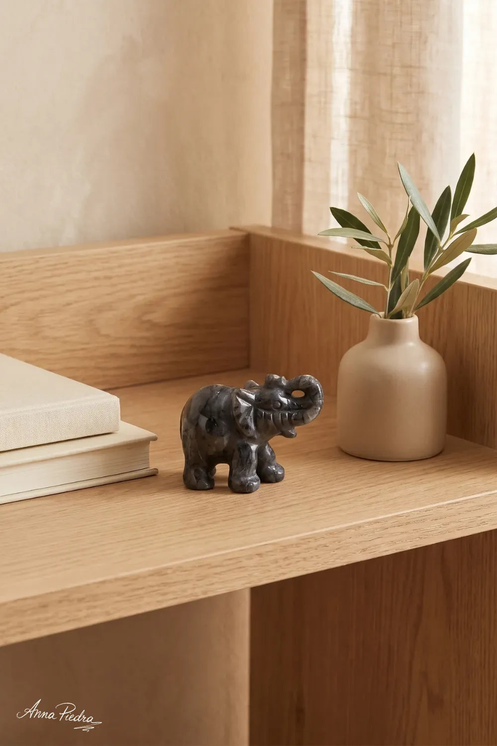 Elefante de la suerte de labradorita sobre una mesita de madera junto a libros y un jarrón con olivo - Anna Piedra